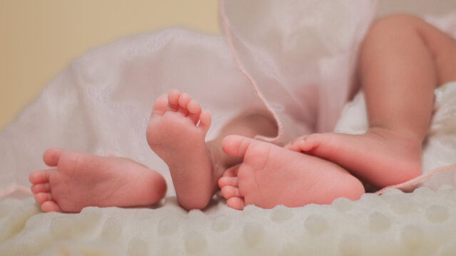 Infant care, feet twin baby, childs, tenderness, family bonding, and early childhood. Close up of newborn baby feet gently supported by an adult hand, with soft natural light and pastel colors.