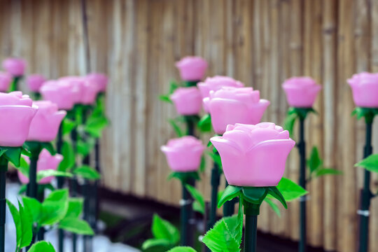 Rows of LED artificial pink rose lights in illuminated garden on artificial snow. LED artificial pink rose lights on dark green stems with fluffy artificial white snow and artificial green grass.