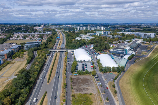Aerial view of busy traffic on M50 motorway in Dublin, Ireland, running alongside sports facility with white inflatable air domes, parking lots and horse racing track with grandstands.