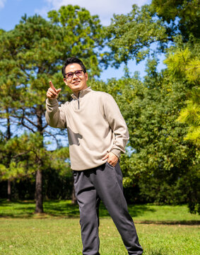 A middle-aged Asian man wearing glasses stands in a park.