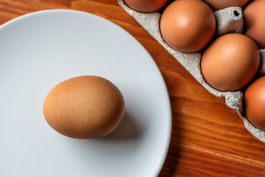 One big extra large raw egg with two yellow yolks, on a white plate on a wooden table.