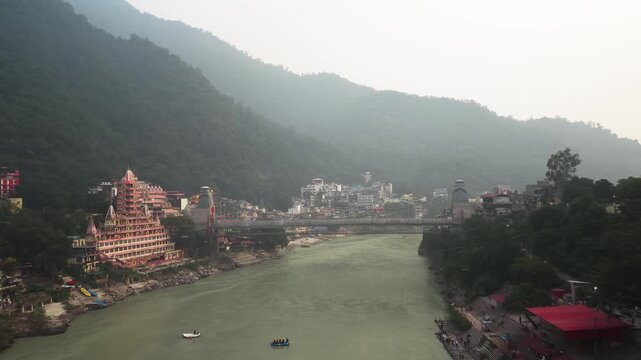 Aerial view of Ganges River flowing through Rishikesh, Uttarakhand, featuring the multi-tiered Tera Manzil Temple (Trayambakeshwar Temple) on the left and a suspension bridge (such as Lakshman Jhula).