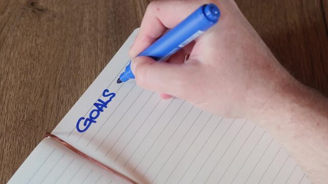A close-up of a human hand writing its main goals and plans for the coming New year in a notebook with a marker.