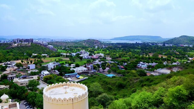 A round cream turret stands in the foreground of a sweeping view across green neighborhoods in Udaipur.