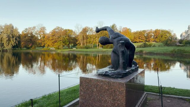 POV walkthrough of an empty autumn park shot on stabilizer. A bronze statue stands by calm waters, creating a peaceful atmosphere. Located in Catherine Park, Pushkin, Saint Petersburg.