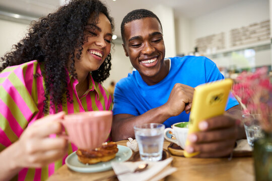 Happy diverse couple sharing smartphone at cafe