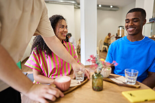 Service personnel bringing coffee to smiling customers in a cafe