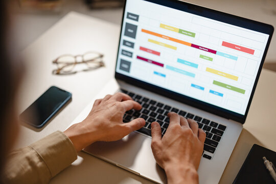 Person Typing on a Laptop With a Colorful Schedule on Screen