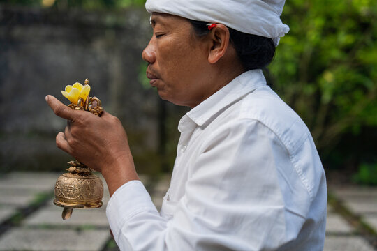 Ceremony in Bali With a Man Holding a Bell and Offering Flowers
