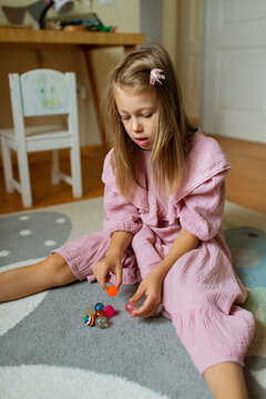 Little girl in pink dress sorts her toys on a playroom rug in bedroom