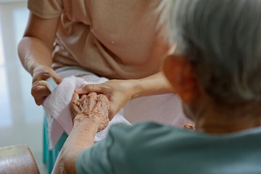 Daughter wiping senior mother's wrinkled fingers with a soft towel