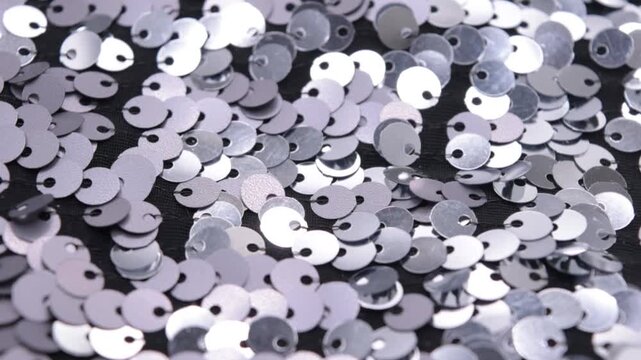 Close-up rotating shot of shimmering silver sequins on black fabric background, highlighting texture and light reflection