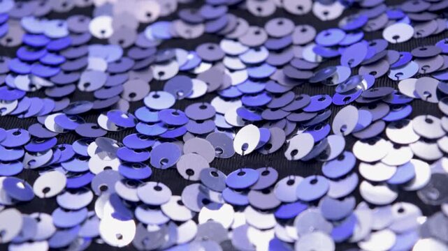 Close-up rotating shot of shimmering silver and blue sequins on black fabric background, highlighting texture and light reflection