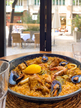 Delicious and authentic Spanish paella mixta with saffron rice, mussels, shrimp, squid, chicken, and a lemon wedge, served in a traditional paella pan on a wooden table  outdoor restaurant terrace.