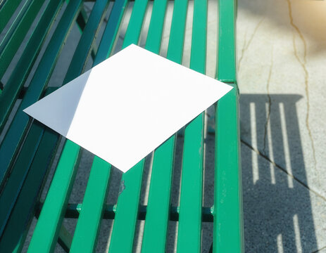 Blank white flyer mockup on a green metal bench in sunlight