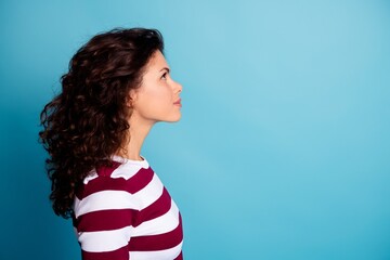 Young woman in profile looking up against a blue background wearing a striped shirt with curly hair, thoughtful expression and clean studio portrait © deagreez
