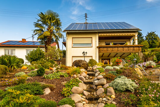House with rooftop solar panels overlooking a rock garden in a residential area