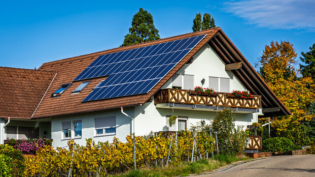 Solar panels cover the roof of a house with a balcony beside a road in autumn