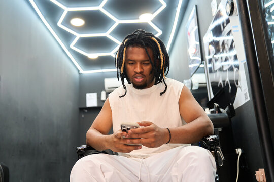 Young black man using smartphone in barbershop