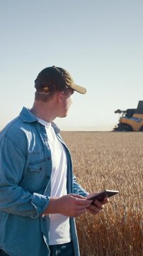 Man farmer uses tablet as combine harvester cuts wheat in field