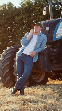 Farmer in shirt chews straw while leans on combine harvester