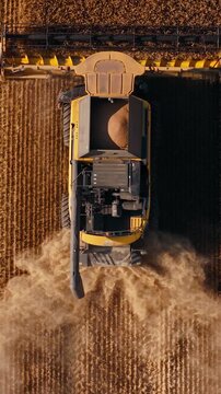 Combine harvester cutting crops through golden field upper view