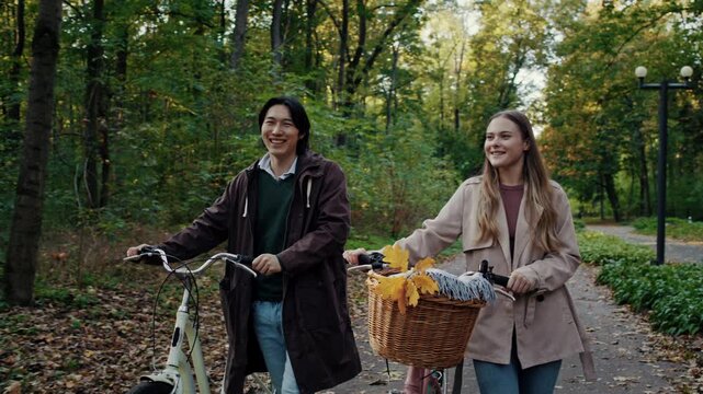 Smiling couple walks bicycles together along autumn park path
