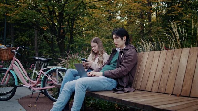 Students couple relaxes on quiet wooden bench by bicycles in park