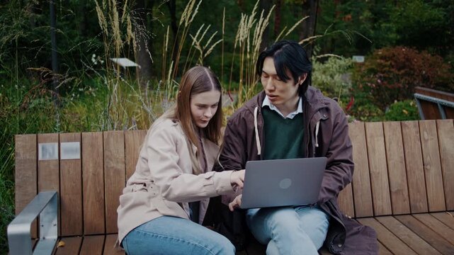 Couple discusses laptop content while sitting on park bench
