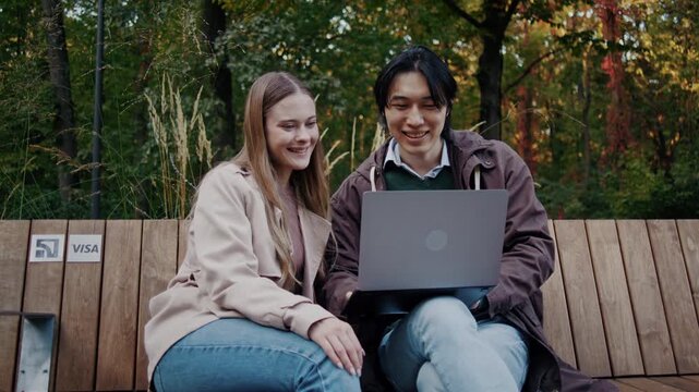 Smiling couple enjoys laptop together on autumn park bench