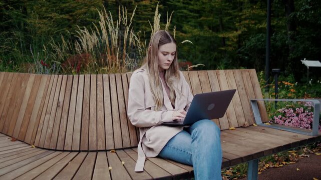 Woman works on laptop alone while sitting on autumn park bench
