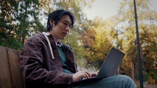 Asian man works remotely on laptop in peaceful autumn park