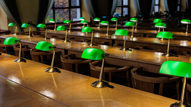 Rows of green banker lamps on wooden desks in empty historic library reading room