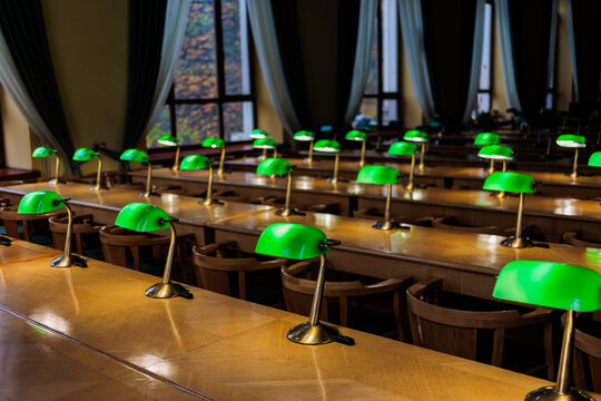 Rows of green banker lamps on wooden desks in empty historic library reading room