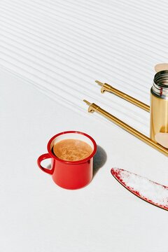 Red enamel mug of steaming cocoa on a groomed snow track with ski gear, a cozy refreshment for winter tourism and cafes with copy space