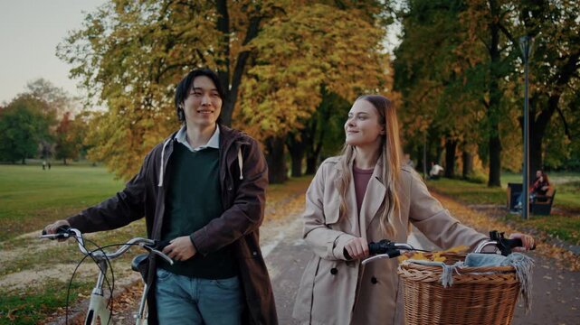 Happy couple walks bicycles talking together on autumn park path