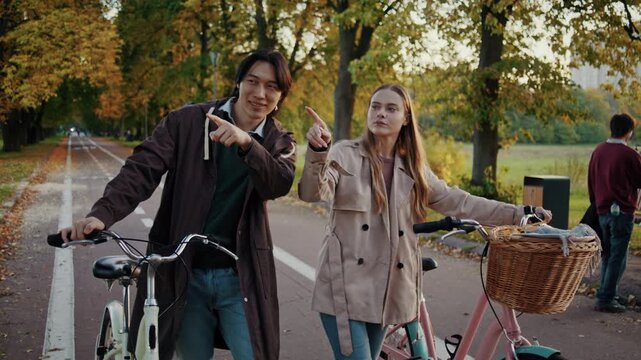Couple points toward route while walking with bicycles in park