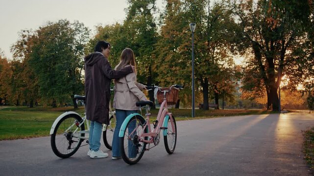 Couple stands near bicycles during sunset walk in autumn park