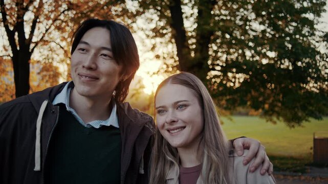 Smiling couple stands close together in autumn sunset park