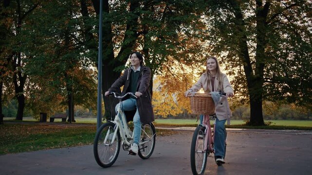 Couple rides bicycles together through autumn park at sunset