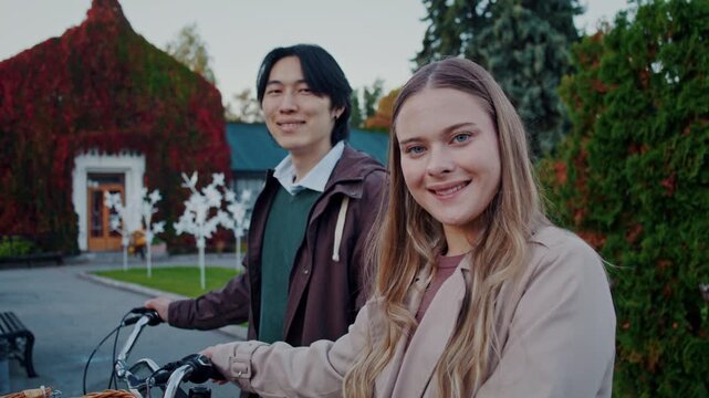 Happy couple smiles standing at bicycles by houses in autumn park