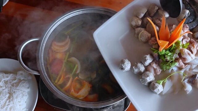 Cooking soup. Seafood and vegetables hot pot served in Asian restaurant. Vietnamese Hot pot cuisine. Steming hot pot over flame at Asian restaurant table.