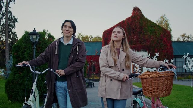 Couple pauses with bicycles looking around autumn garden