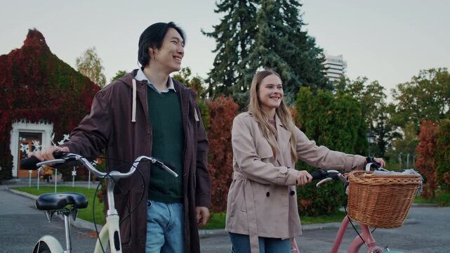 Cheerful couple walks bicycles together through autumn park