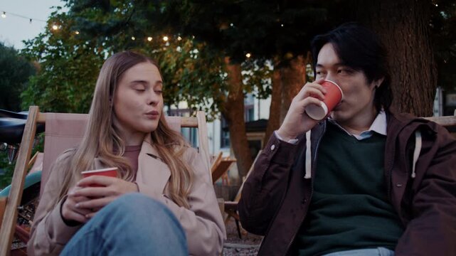 Couple talks holding hot drinks as resting near parked bicycles