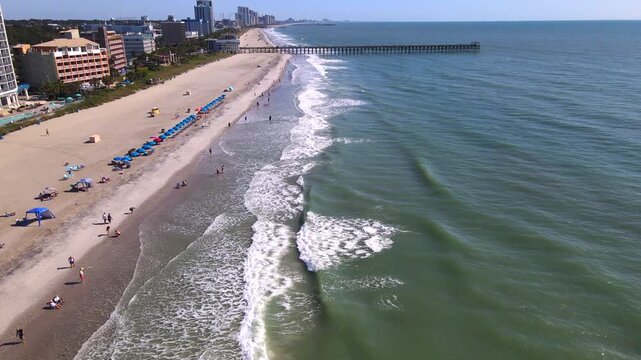 Foamy wave crests roll toward beachgoers as the drone approaches a Myrtle Beach pier.