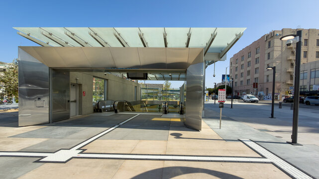 LOS ANGELES, CA, JUL 30, 2026: Wilshire La Brea station entrance with glass canopy, stainless steel portal and escalators descending, tactile paving in front, and pink historic building across street