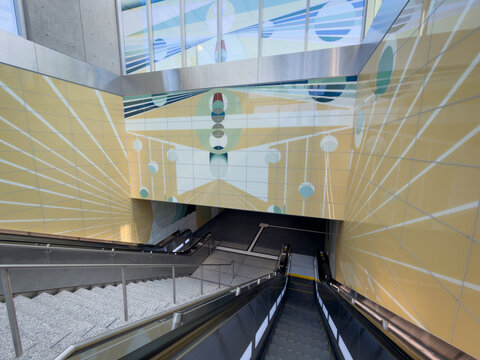 LOS ANGELES, CA, JUL 30, 2026: View down the escalators and granite stairs at Wilshire La Brea station, framed by a yellow glass-tile mural of radiating lines, circles and blue-green geometric forms