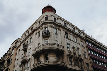 A grand corner building features curved balconies, ornate stonework and a red rooftop turret. Period architecture inspires heritage tourism and restoration themes. © Ekaterina