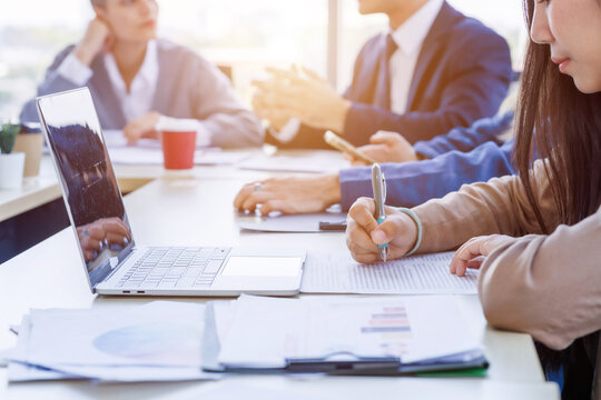 Close-up of businesswoman taking notes during corporate meeting with laptop on table.blurred colleagues and executives sit around the conference table business plans in a bright office